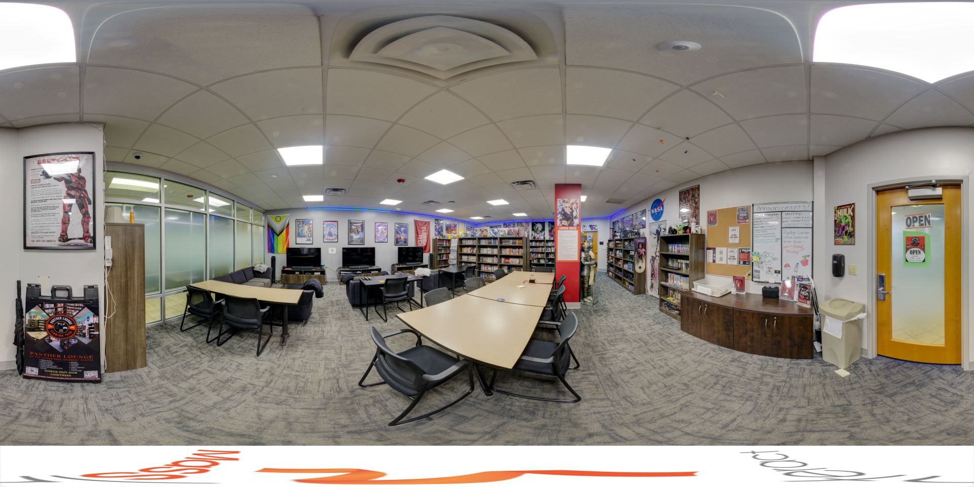 A panoramic view of the Panther Lounge at Florida Tech, featuring tables and chairs for studying, bookshelves filled with books, posters on the walls, and a television area. The room has a comfortable and welcoming atmosphere with various decorations and amenities for students